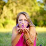 woman wearing pink sleeveless top blowing purple flowers