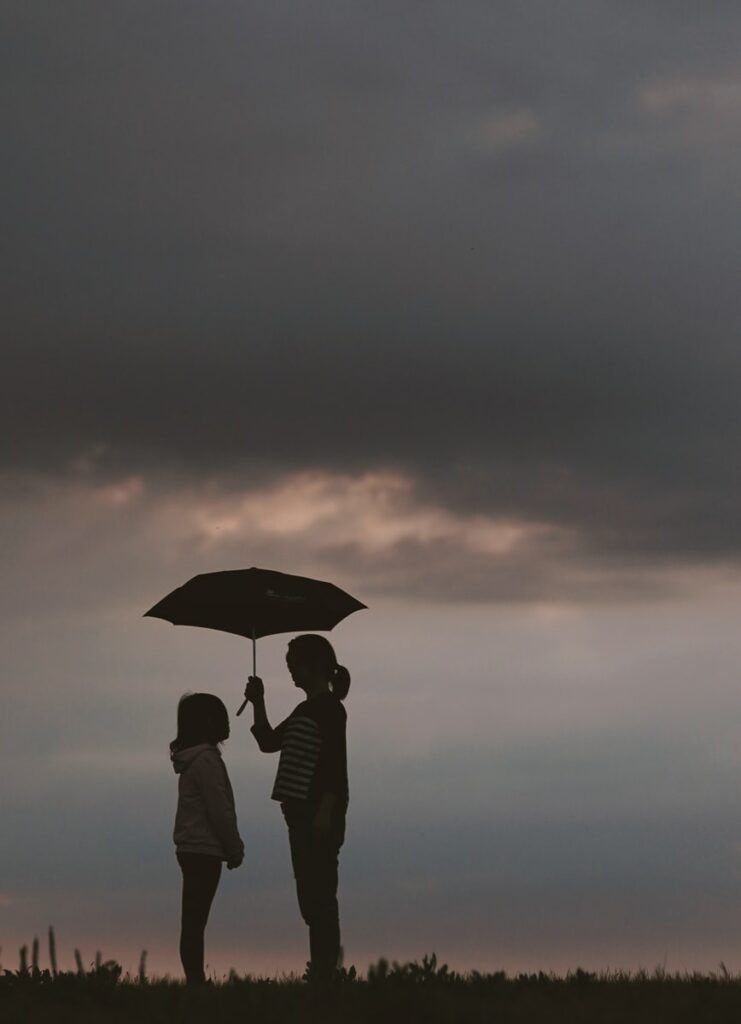 silhouette of woman holding umbrella standing in front of girl on hill during night time