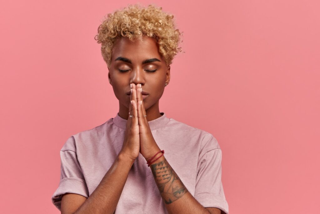 grateful hopeful young black woman stands meditative pose enjoys peaceful atmosphere holds hands praying gesture isolated pink background has sense inner peace meditation concept