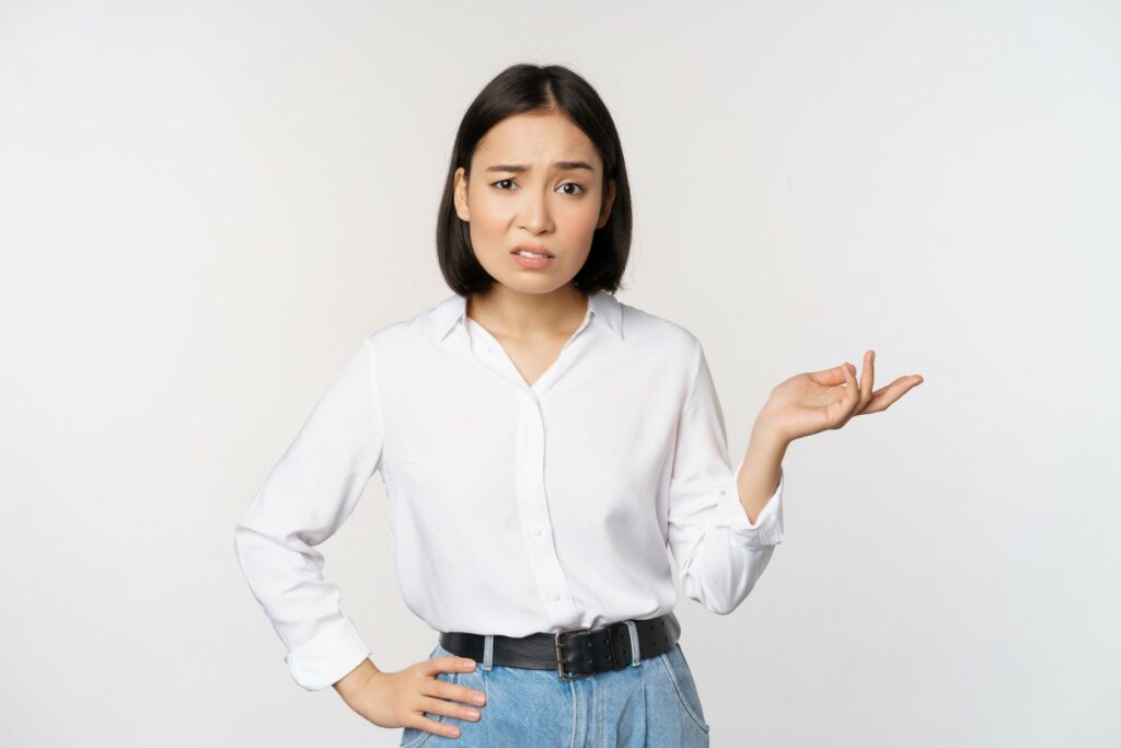portrait confused asian woman asking so what whats your problem gesture staring puzzled clueless annoyed standing white background
