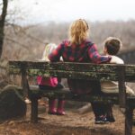 woman between two childrens sitting on brown wooden bench during daytime